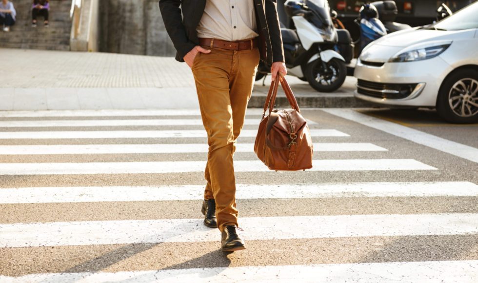 Cropped photo of stylish successful man in business wear walking through pedestrian crossing in downtown with leather male bag in hand